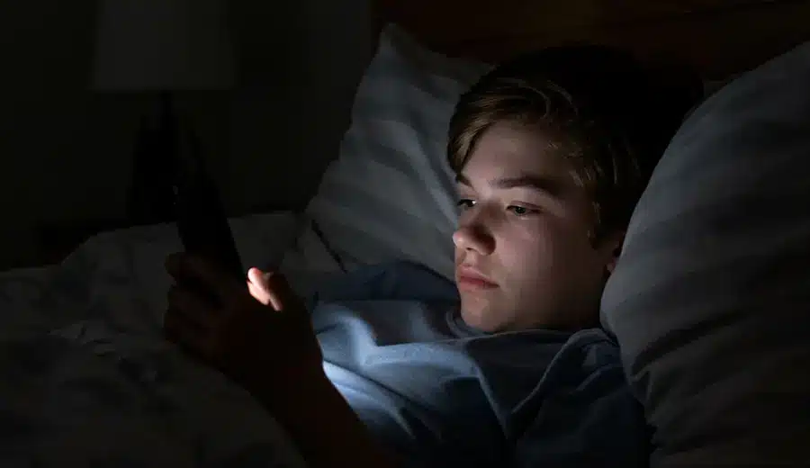Young man lying in bed at night, looking at his phone.